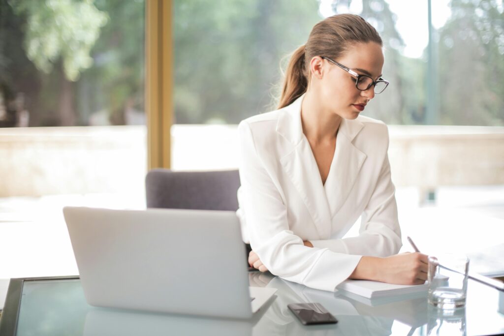 woman in white suit with glasses working on her computer making a business plan